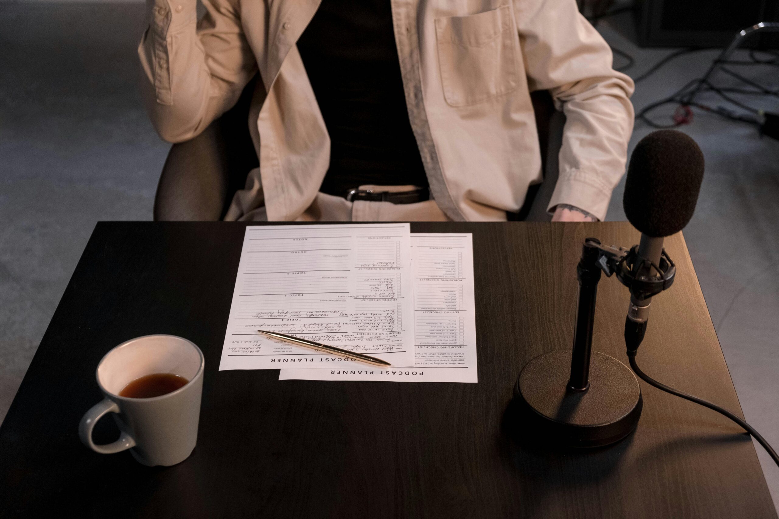 Person Sitting by Table with Papers and Microphone